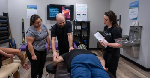 A group of students attentively watches Dr. Christopher Allin as he performs a neuromyofascial therapy technique on a patient.