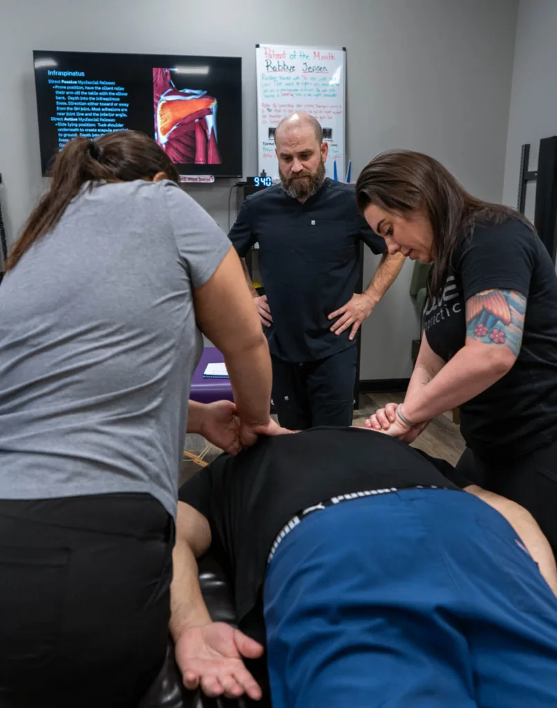 Two students practice a neuromyofascial therapy technique under the guidance of Dr. Christopher Allin in a hands-on training session.